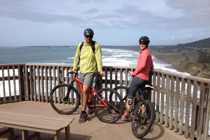 Two bikers leaning against lookout platform overlooking the sea
